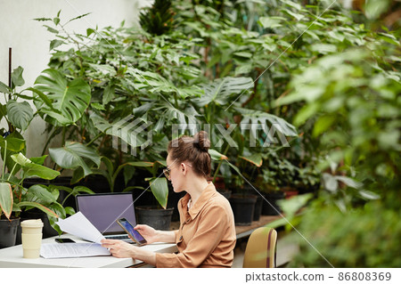 Young businesswoman scrolling in smartphone by workplace Young businesswoman scrolling in smartphone by workplace 86808369