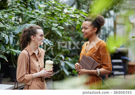 Happy young female with drink consulting with confident florist Happy young female with drink consulting with confident florist 86808393
