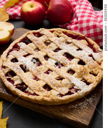 baked round traditional apple pie on brown wooden board and fresh red apples, top view baked round traditional apple pie on brown wooden board and fresh red apples, top view 86808498