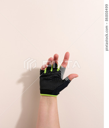 black sports glove on a female hand, beige background. Part of the body is lifted up 86808499