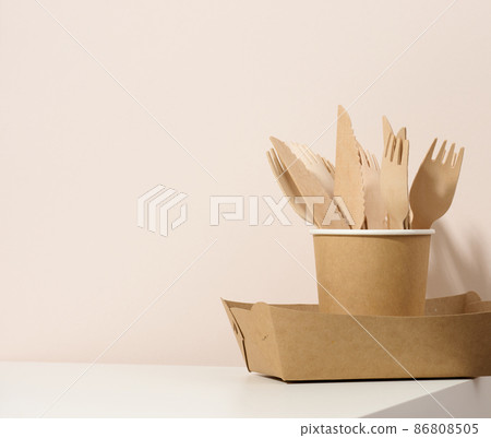 paper cardboard brown plates and cups, wooden forks and knives on a white table, beige background. Eco-friendly tableware, zero waste paper cardboard brown plates and cups, wooden forks and knives on a white table, beige background. Eco-friendly tableware, zero waste 86808505