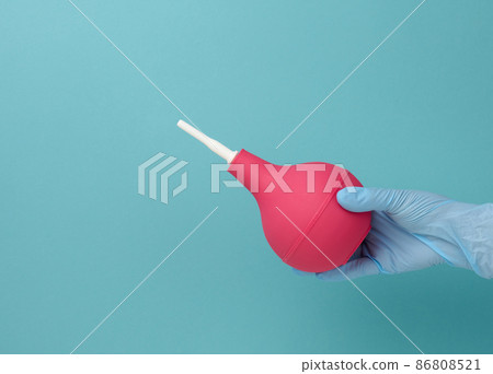 a hand in a blue medical glove holds a pink rubber enema on a blue background a hand in a blue medical glove holds a pink rubber enema on a blue background 86808521