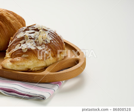 Baked crisp croissant on wooden board, white table. Breakfast 86808528