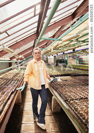 Young pretty female worker of large green house having rest Young pretty female worker of large green house having rest 86808585