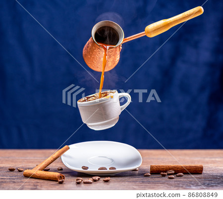 Levitation of pouring coffee from a cezve into a cup with a splash. 86808849