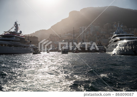 A lot of huge yachts are in port Hercule of Monaco at sunset, mountain is on background, magic backlight is on glossy boards of the motor boats, megayachts are moored in marina, sun reflections A lot of huge yachts are in port Hercule of Monaco at sunset, mountain is on background, magic backlight is on glossy boards of the motor boats, megayachts are moored in marina, sun reflections 86809087