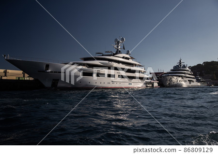 Two huge yacht in port of Monaco at sunset, glossy board of the motor boat, the chrome plated handrail, megayacht is moored in marina, sun reflection on glossy board, mountain is on background 86809129