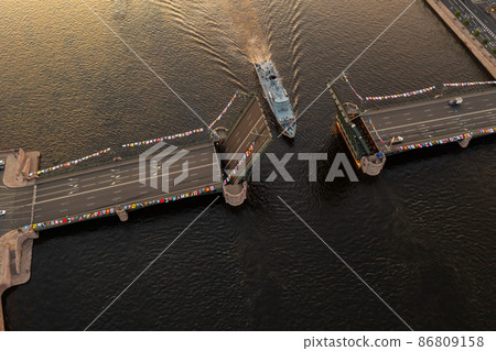 Aerial landscape of warship pass under a raised Palace drawbridge, top view, black color of water, the Neva River before the holiday of the Russian Navy at early morning Aerial landscape of warship pass under a raised Palace drawbridge, top view, black color of water, the Neva River before the holiday of the Russian Navy at early morning 86809158