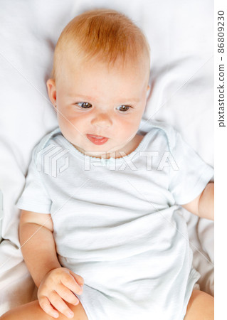 Cute little newborn girl with smiling face looking at camera on white background. Infant baby resting playing lying down on crib bed at home. Motherhood happy child concept Cute little newborn girl with smiling face looking at camera on white background. Infant baby resting playing lying down on crib bed at home. Motherhood happy child concept 86809230