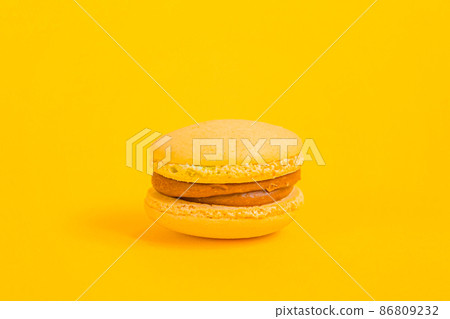 Sweet almond colorful yellow macaron or macaroon dessert cake isolated on trendy yellow modern fashion background. French sweet cookie. Minimal food bakery concept. Copy space Sweet almond colorful yellow macaron or macaroon dessert cake isolated on trendy yellow modern fashion background. French sweet cookie. Minimal food bakery concept. Copy space 86809232