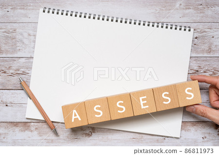 Building blocks, pens, notebooks, human hands with "ASSESS" written on them 86811973