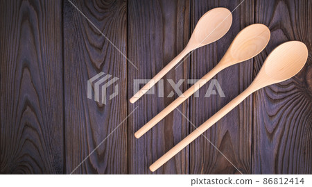 Three wooden spoons on a dark wood table. 86812414
