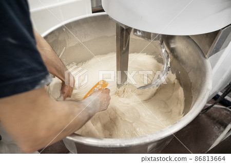 Baker taking out dough of a kneading machine at industrial bakery 86813664