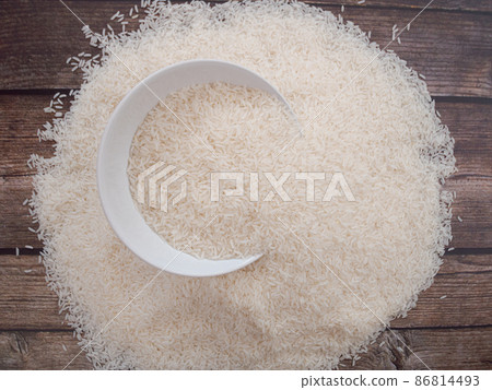 Close up top view rice in a white bowl and scattered near on wooden table with copy space for text and design Close up top view rice in a white bowl and scattered near on wooden table with copy space for text and design 86814493