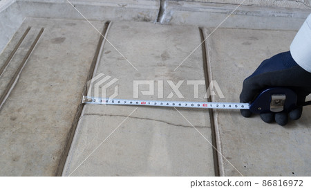 A worker who measures the crack dimensions of a concrete floor. 86816972