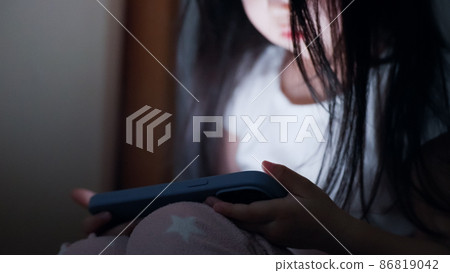 A 4-year-old child looking at a smartphone in a dark room at night 86819042