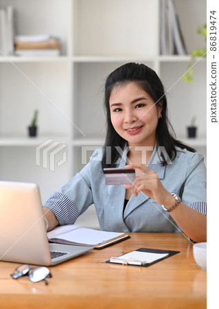Portrait young asian woman holing credit card and using computer laptop for payment online. 86819474