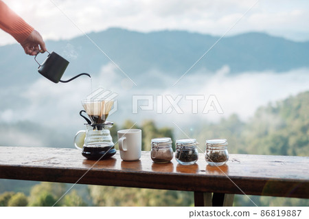 Hand pouring Hot water during brewing arabica coffee by Vintage coffee drip equipment on wooden table in the morning with mountain and nature background Hand pouring Hot water during brewing arabica coffee by Vintage coffee drip equipment on wooden table in the morning with mountain and nature background 86819887