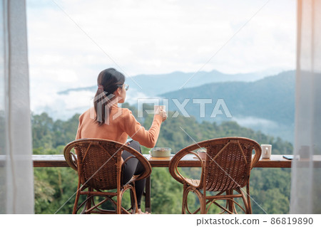 Happy woman drinking coffee and eating breakfast against mountain view at countryside home or homestay in the morning. Vacation, blogger, SoloTravel, journey, trip and relaxing concept 86819890
