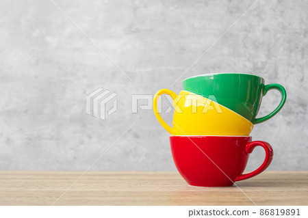 stack of colorful coffee cups on wall background at cafe. Green, yellow and red color ceramic mug on table at home. International coffee day concept stack of colorful coffee cups on wall background at cafe. Green, yellow and red color ceramic mug on table at home. International coffee day concept 86819891
