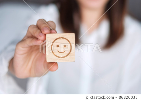 Happy Woman holding smile emotion face block. Customer choose Emoticon for user reviews. Service rating, mental health, positive thinking, satisfaction, evaluation and feedback concept Happy Woman holding smile emotion face block. Customer choose Emoticon for user reviews. Service rating, mental health, positive thinking, satisfaction, evaluation and feedback concept 86820033