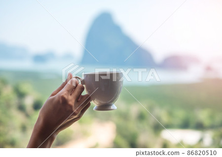 happy woman in bathrobe holding hot coffee cup or tea mug after waking up and enjoy Phang Nga bay view point, Tourist relaxing in tropical resort at Samet Nang She. Travel summer vacation concept 86820510