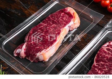 Raw steak of marbled beef in vacuum plastic pack, on old dark wooden table background Raw steak of marbled beef in vacuum plastic pack, on old dark wooden table background 86820528