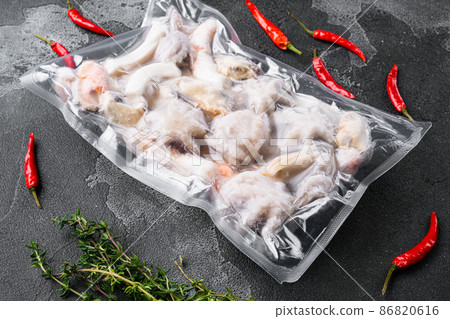 Frozen seafood set, squid rings, shrimp and octopus vacuum Packed, on black dark stone table background 86820616