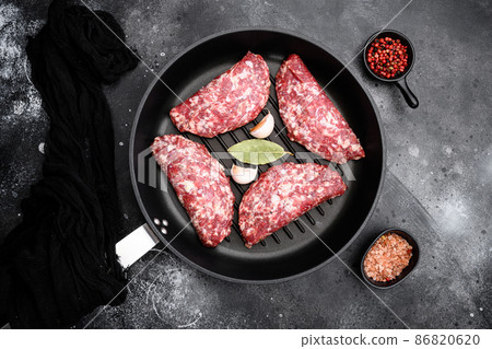 Ground raw meat patties. Meat cutlet ready to cook. Farm organic meat, in cast iron frying pan, on black dark stone table background, top view flat lay Ground raw meat patties. Meat cutlet ready to cook. Farm organic meat, in cast iron frying pan, on black dark stone table background, top view flat lay 86820620