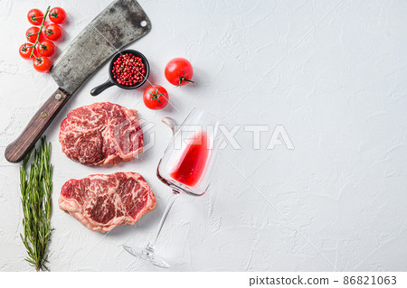 Organic top blade steak, raw beef meat with seasonings, rosemary, garnet, rose wine glass and butcher cleaver. White textured background. Top view with space for text. Organic top blade steak, raw beef meat with seasonings, rosemary, garnet, rose wine glass and butcher cleaver. White textured background. Top view with space for text. 86821063