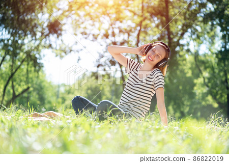 Young woman happens to have music in a summer park Young woman happens to have music in a summer park 86822019