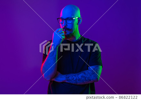 Young bald man using electronic cigarette, vaping in studio. color filters. Vaping concept Young bald man using electronic cigarette, vaping in studio. color filters. Vaping concept 86822122