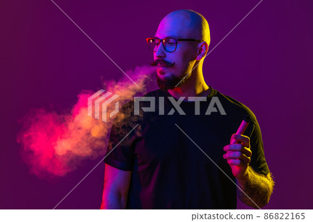 Handsome adult bald man is vaping, blowing smoke in studio. color filters. Vaping concept  86822165