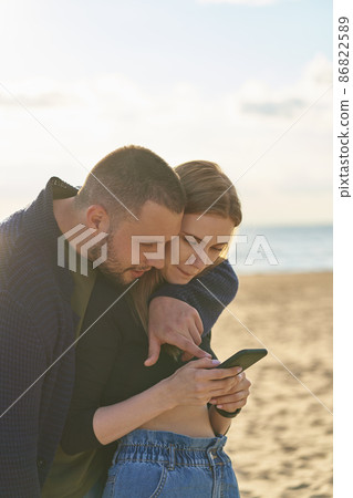 Young couple standing on sandy beach and looking at smartphone, man points finger at mobile Young couple standing on sandy beach and looking at smartphone, man points finger at mobile 86822589