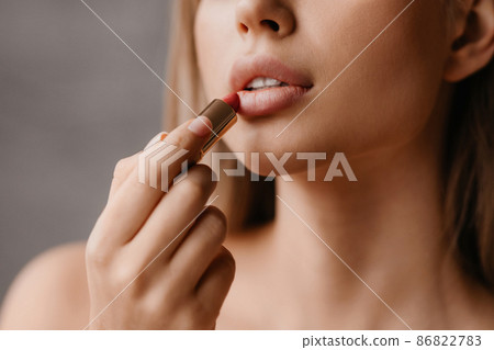 Lip skincare and beauty treatments concept. Young woman with perfect skin applying nude lipstick, doing morning routine 86822783