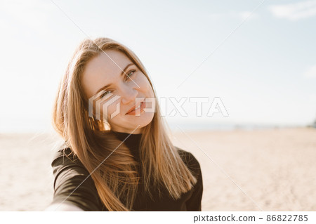 Pretty woman with long hair takes selfie on smartphone on beach in summer or autumn. Pretty woman with long hair takes selfie on smartphone on beach in summer or autumn. 86822785