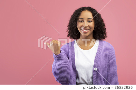 Cool young black woman in casual wear pointing aside, offering copy space for your ad design on pink studio background 86822926