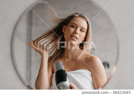 Haircare. Young woman drying and styling hair with hairdryer, making hairstyle after morning shower 86823065