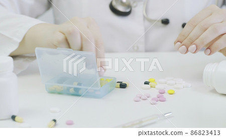 Close-up of a pillbox with different tablets. A person's hands put pills in a pillbox 86823413