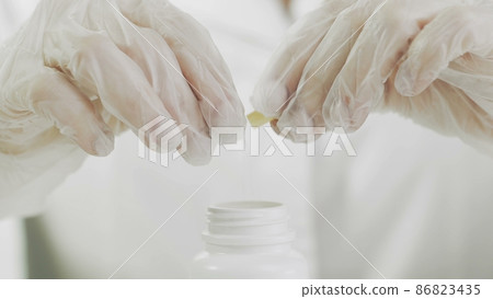 A woman opens a yellow medical capsule and spills yellow powder from it A woman opens a yellow medical capsule and spills yellow powder from it 86823435