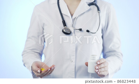 Close-up of an unrecognizable woman, a doctor, holding a jar of pills and throwing it into her hand 86823448