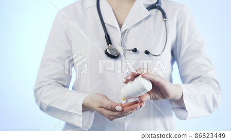 Close-up of an unrecognizable woman, a doctor, holding a jar of pills and throwing it into her hand 86823449