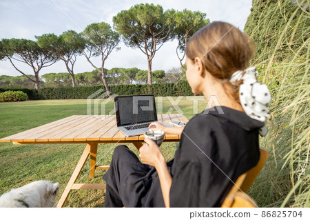 Girl use laptop and drink tea at table on lawn Girl use laptop and drink tea at table on lawn 86825704