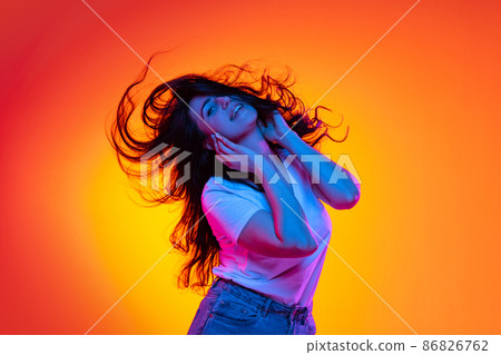 Excited young beautiful caucasian girl with long dark hair dancing isolated on orange background in neon light, filter. Concept of emotions, ads, sale Excited young beautiful caucasian girl with long dark hair dancing isolated on orange background in neon light, filter. Concept of emotions, ads, sale 86826762