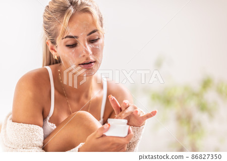 Beautiful girl applies skincare product from a glass jar on her face 86827350