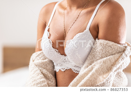 Beautiful cleavage of a young woman with a white bra. Woman in lingerie sitting on the bed in the bedroom Beautiful cleavage of a young woman with a white bra. Woman in lingerie sitting on the bed in the bedroom 86827353