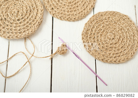 crocheting jute coasters, eco natural home decor. hand made coasters on a table, knitting process. DIY kitchen accessories made of jute. 86829082