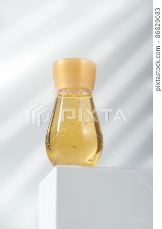 a bottle of cosmetic liquid with golden sparkles on white podium or pedestal. enzyme solution for face skin peeling. beauty care and cosmetology. 86829083
