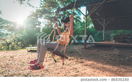Little Boy is swinging in a campingground swing freely, with sun and wood in the background. Little Boy is swinging in a campingground swing freely, with sun and wood in the background. 86830280