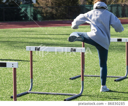 Runner perfoming trail leg hurdle drills on a green turf field Runner perfoming trail leg hurdle drills on a green turf field 86830285